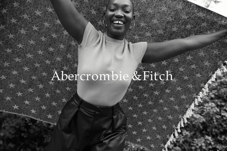 Smiling African-American woman outdoors, holding a patterned blanket in a fashion shot for Abercrombie & Fitch with a monochrome aesthetic.