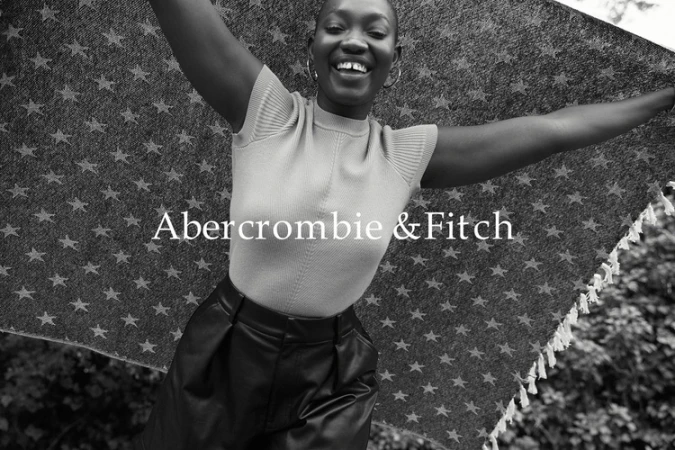 Smiling African-American woman outdoors, holding a patterned blanket in a fashion shot for Abercrombie & Fitch with a monochrome aesthetic.