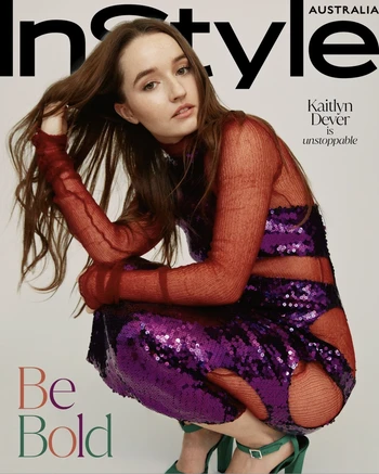 Kaitlyn Dever on the cover of InStyle Australia magazine, wearing a sequined dress and green shoes, kneeling indoors against a white backdrop.