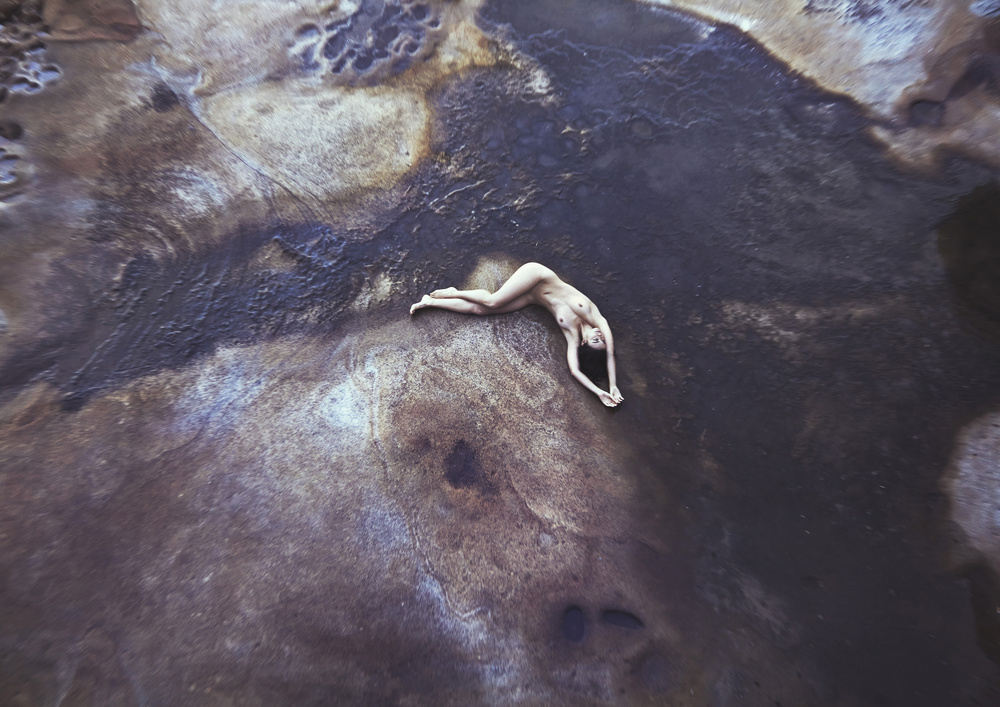Aerial view of a woman lying on textured ground with dark earth tones and mineral deposits