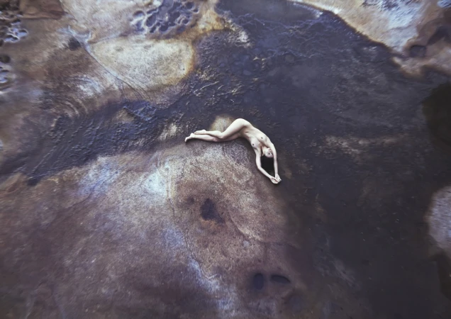 Aerial view of a woman lying on textured ground with dark earth tones and mineral deposits