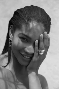 Black and white portrait of an adult woman with hand on face, wet hair, and ring jewelry against a bright, neutral backdrop.