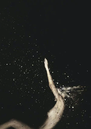 A woman with fair skin and blonde hair raises her arm in front of a dark, cosmic background with glittering bokeh lights.