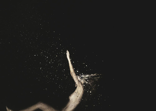 An ethereal image shows an adult woman with outstretched arm surrounded by light particles against a solid black background.