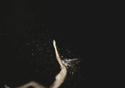An ethereal image shows an adult woman with outstretched arm surrounded by light particles against a solid black background.