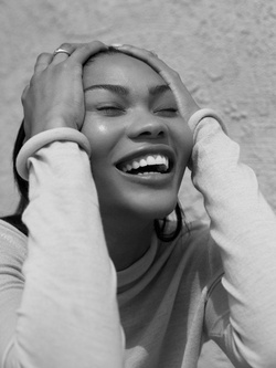 Black and white portrait of a smiling woman holding her hands to her head against a textured background.