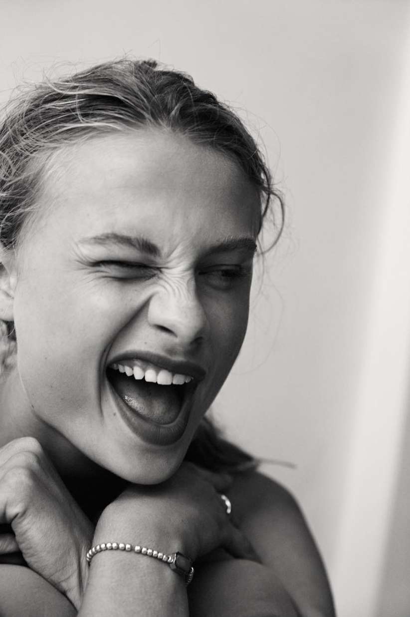 Close up monochrome portrait of a woman laughing with her eyes scrunched shut, photographed by Sylve Colless.