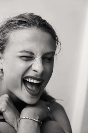 Close up monochrome portrait of a woman laughing with her eyes scrunched shut, photographed by Sylve Colless.