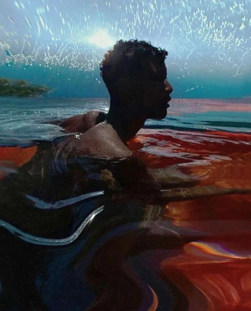 Adult man in water with orange fabric, ocean backdrop. Side view portrait with dark hair, ripples, and splashes in an aquatic scene.