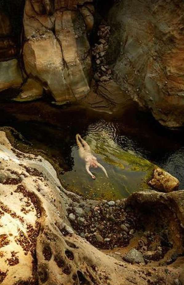 Adult female swims in a natural rock pool surrounded by sandstone formations; overhead shot of a water-filled canyon.