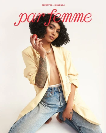 Magazine cover featuring a woman with curly hair wearing a blazer and jeans, holding a strawberry in front of a plain background.