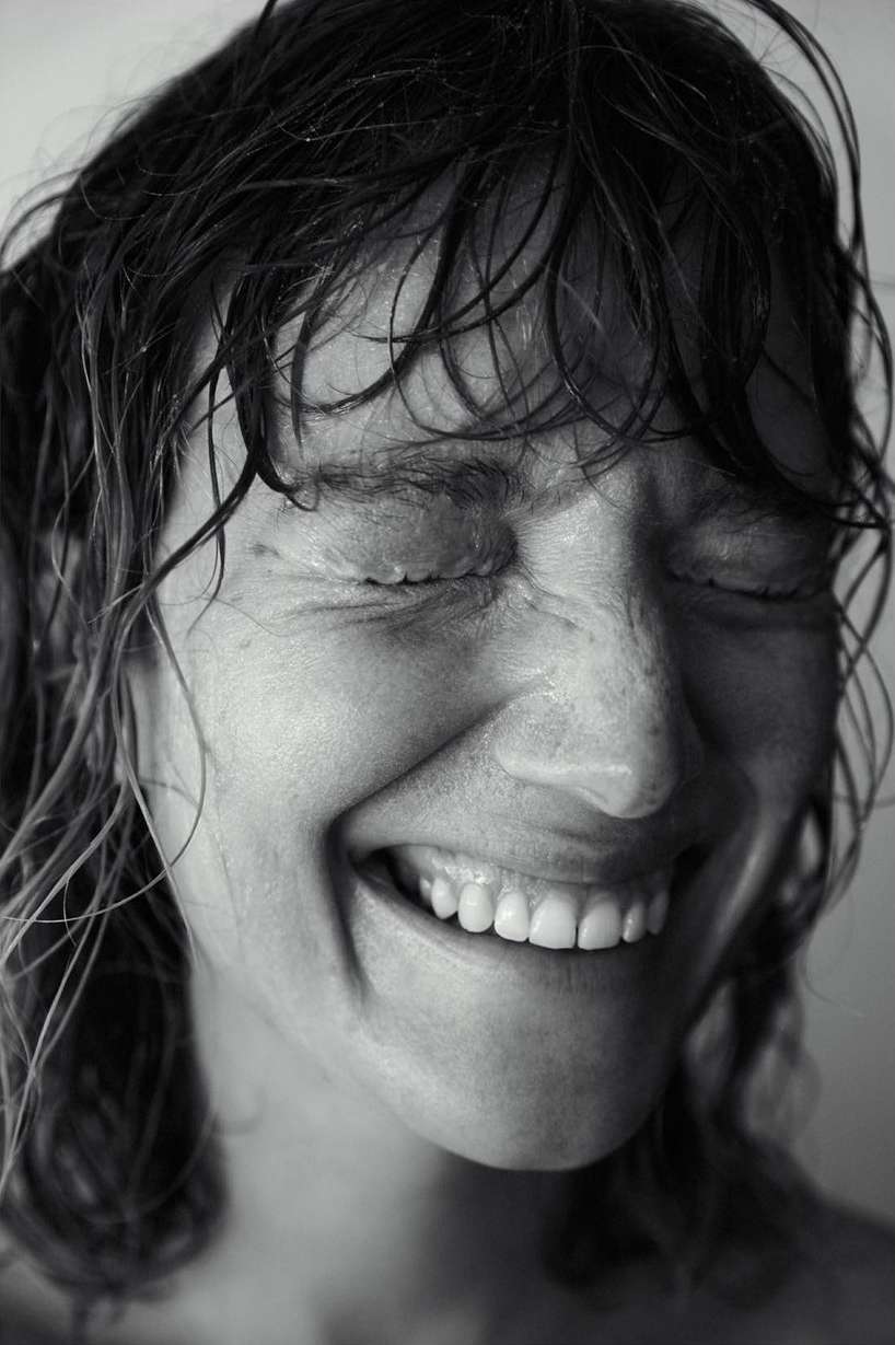 Black and white portrait of a woman with wet hair smiling with her eyes closed, showcasing a joyful and intimate facial expression.