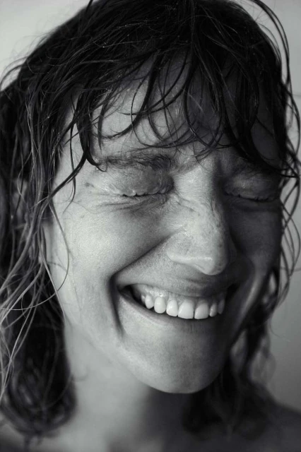 Black and white portrait of a woman with wet hair smiling with her eyes closed, showcasing a joyful and intimate facial expression.