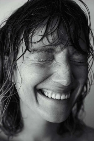 Black and white portrait of a woman with wet hair smiling with her eyes closed, showcasing a joyful and intimate facial expression.