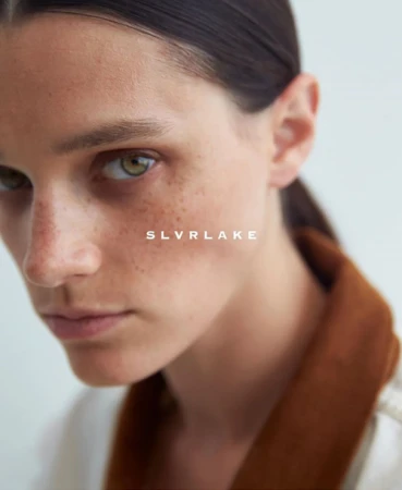 Close-up portrait of a woman with freckles wearing a brown garment against a plain light background by Sylve Colless.