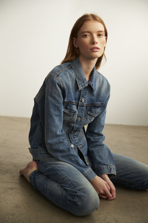 Red-haired woman wearing denim jacket and jeans kneeling on concrete floor