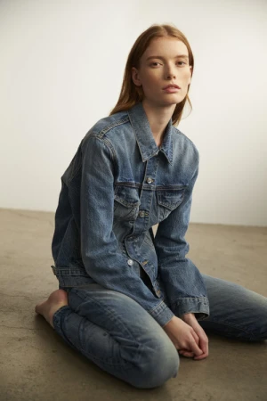 Red-haired woman wearing denim jacket and jeans kneeling on concrete floor