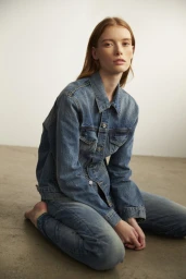 Red-haired woman wearing denim jacket and jeans kneeling on concrete floor
