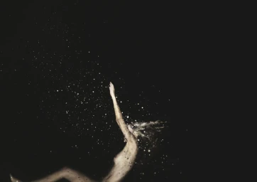 Figure submerged in dark water surrounded by floating droplets and bubbles against black background