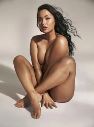 A woman with dark hair seated with knees drawn up against a neutral studio background