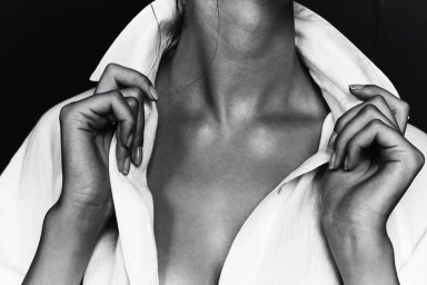 Monochrome portrait of a person holding the collar of a white shirt against a dark background