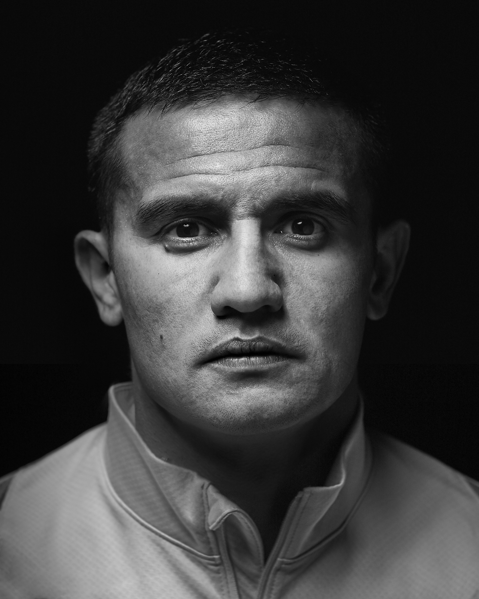 Black and white portrait of a man with short dark hair looking directly at the camera against a dark background, wearing a collared shirt.