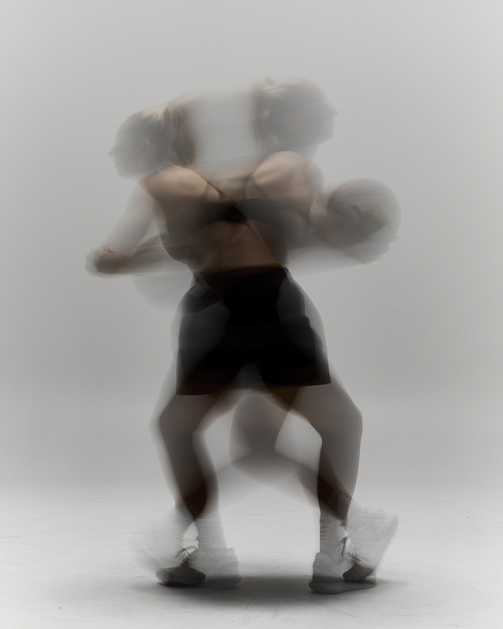 Motion blur image of a woman with athletic build in black workout clothes, posing with a basketball on a white background in a photo studio.