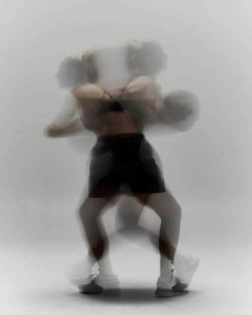 Motion blur image of a woman with athletic build in black workout clothes, posing with a basketball on a white background in a photo studio.