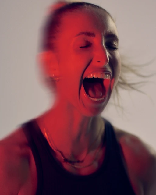 Dynamic, close-up portrait of a woman with an open mouth, expressive face, and dynamic blurred motion, set against a bright background.
