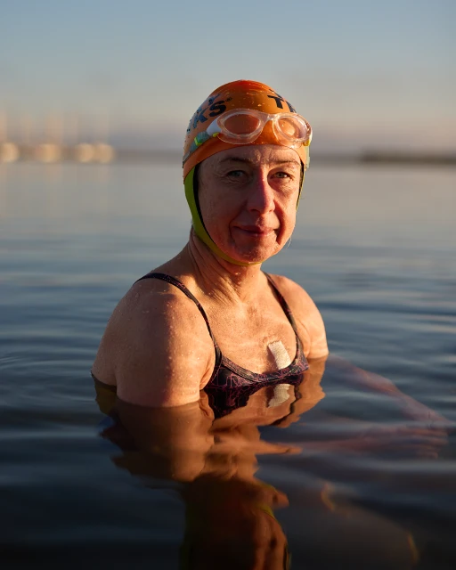 Woman swimmer in outdoor water wearing swim cap, goggles, and bathing suit; water reflects light, creating a serene atmosphere.