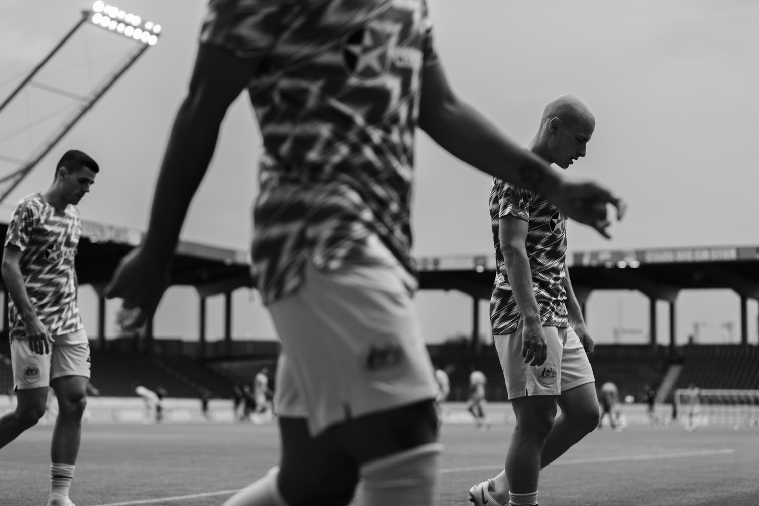 Black and white image of three soccer players in matching patterned shirts and shorts walking on a field during the daytime.