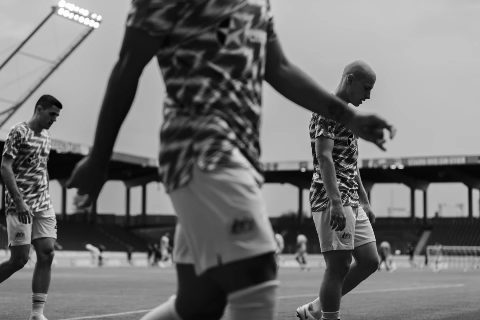 Black and white image of three soccer players in matching patterned shirts and shorts walking on a field during the daytime.