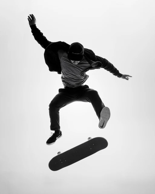 Black and white action shot of a skateboarder in mid-air, skateboard floating below, against a bright white background.