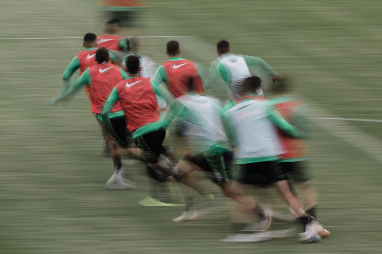 A group of soccer players run across the field during a game, motion blur, red and green uniforms, Nike logo, outdoor setting, daytime.