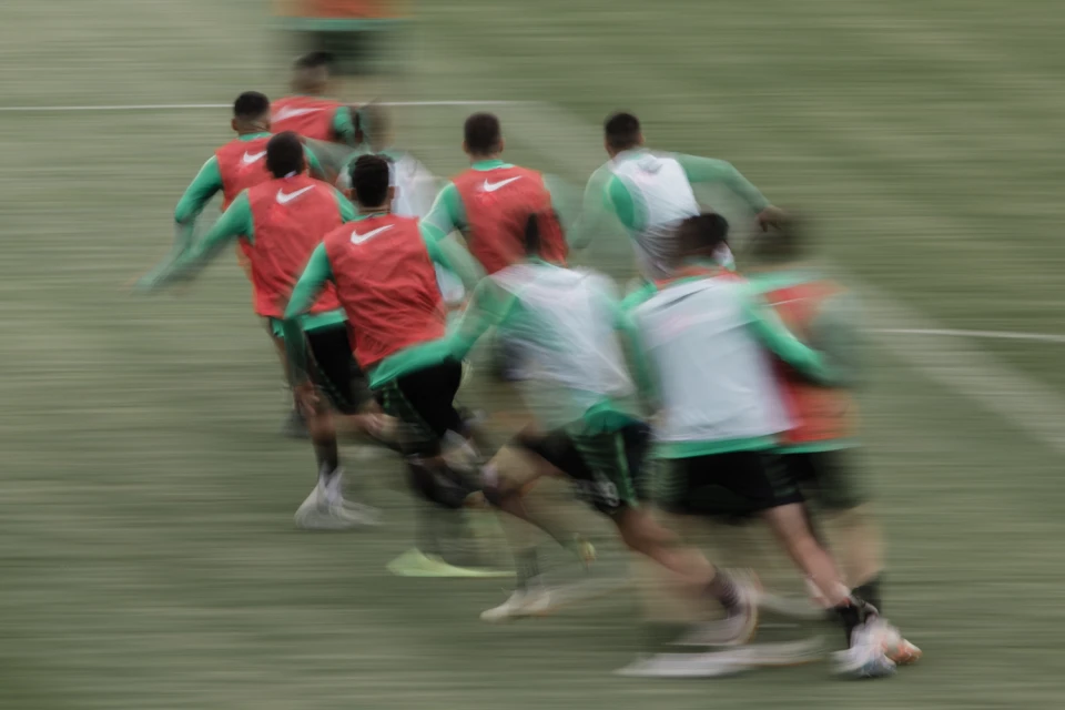 A group of soccer players run across the field during a game, motion blur, red and green uniforms, Nike logo, outdoor setting, daytime.
