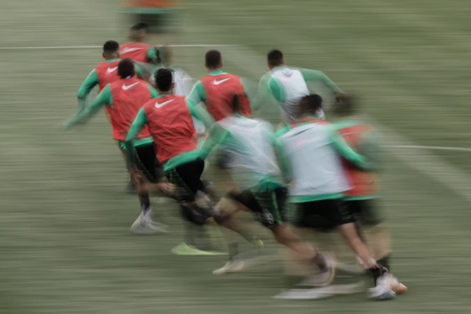 A group of soccer players run across the field during a game, motion blur, red and green uniforms, Nike logo, outdoor setting, daytime.