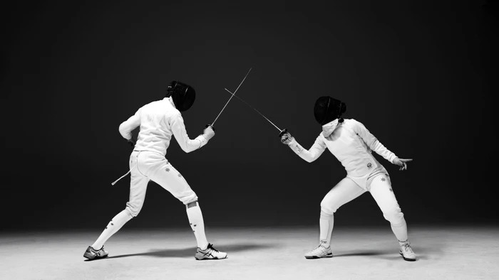 Two fencers in full white uniforms and protective masks crossing foils in a studio setting by Daniel Mazzarella