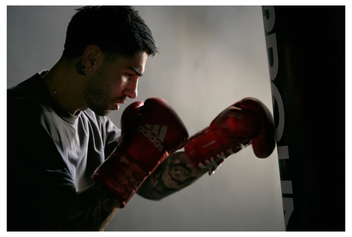Man wearing red boxing gloves throwing a punch at a black heavy bag in a studio setting.