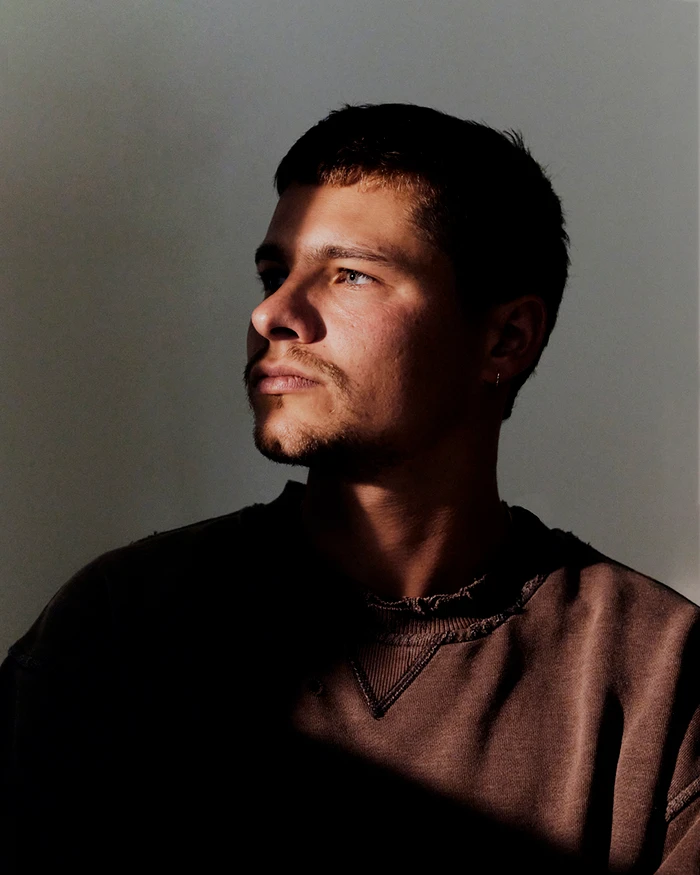 Portrait of a man in a brown sweatshirt lit by sharp sunlight against a grey background