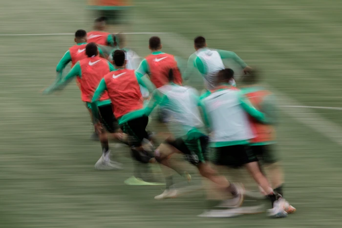 Group of athletes in red and green sports bibs running across a pitch captured with motion blur.
