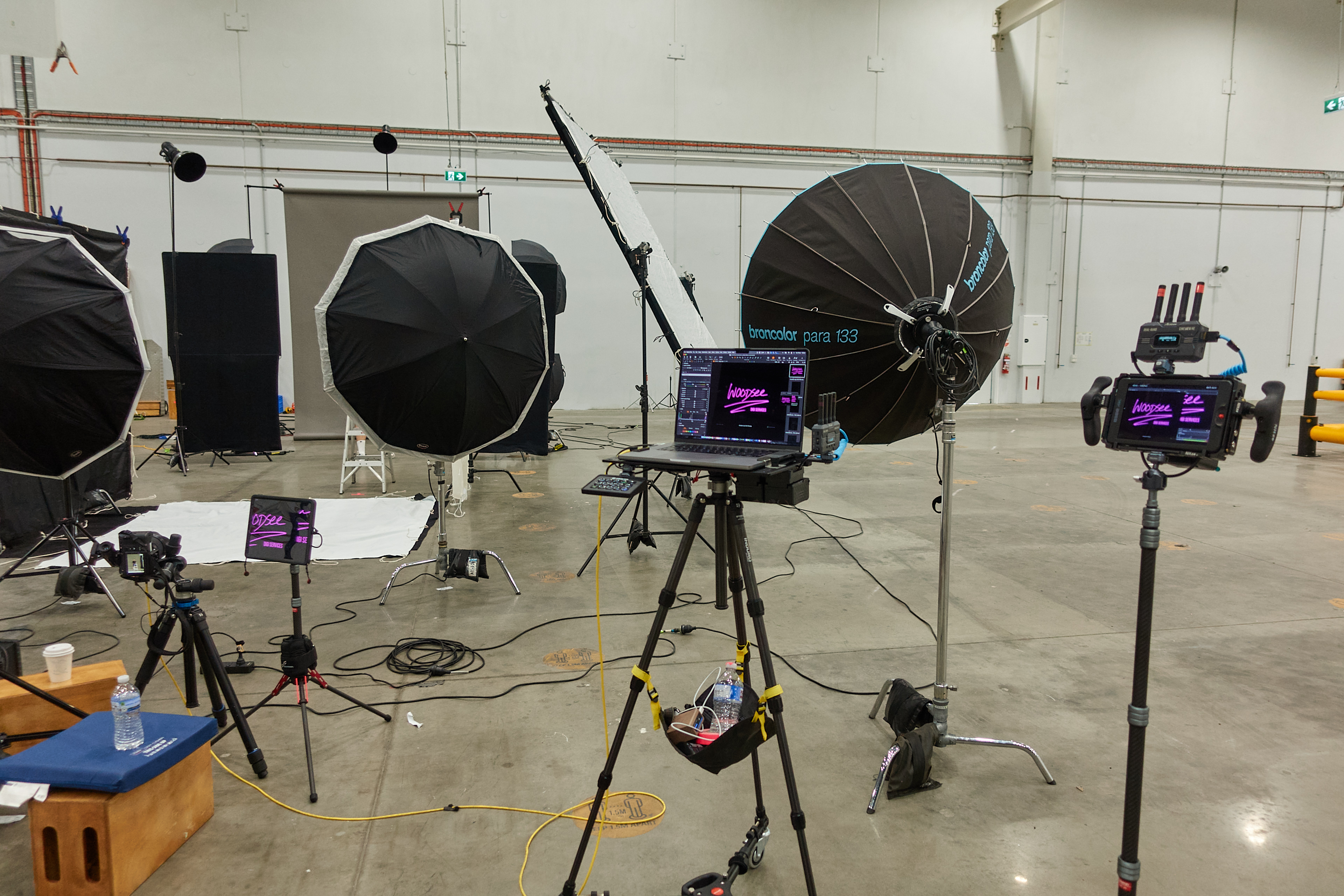 Photo studio setup with umbrellas, screens, cameras, and laptops on tripods, creating a backstage view of a professional photoshoot.
