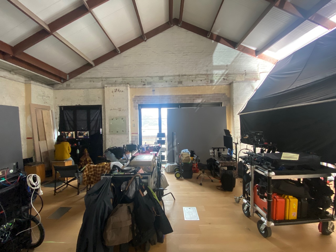 Film set with equipment, cameras, lighting, and crew members in a spacious interior location during daytime, set up for filming.