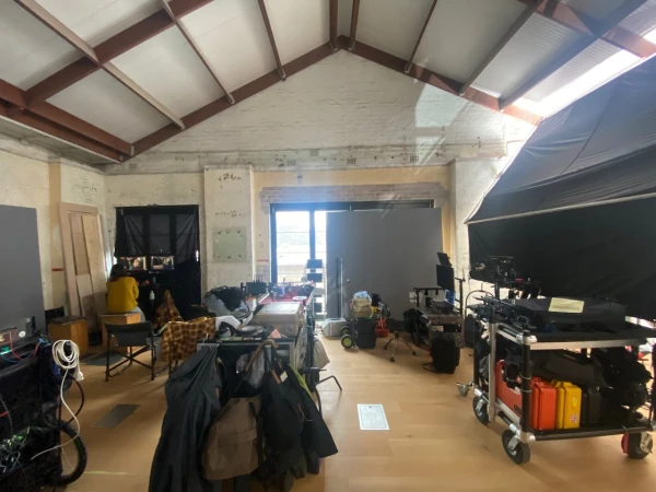 Film set with equipment, cameras, lighting, and crew members in a spacious interior location during daytime, set up for filming.