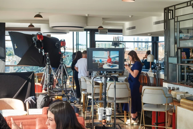 Film crew on set with monitor, lighting equipment, and talent in modern studio or rooftop space, capturing commercial or editorial content.