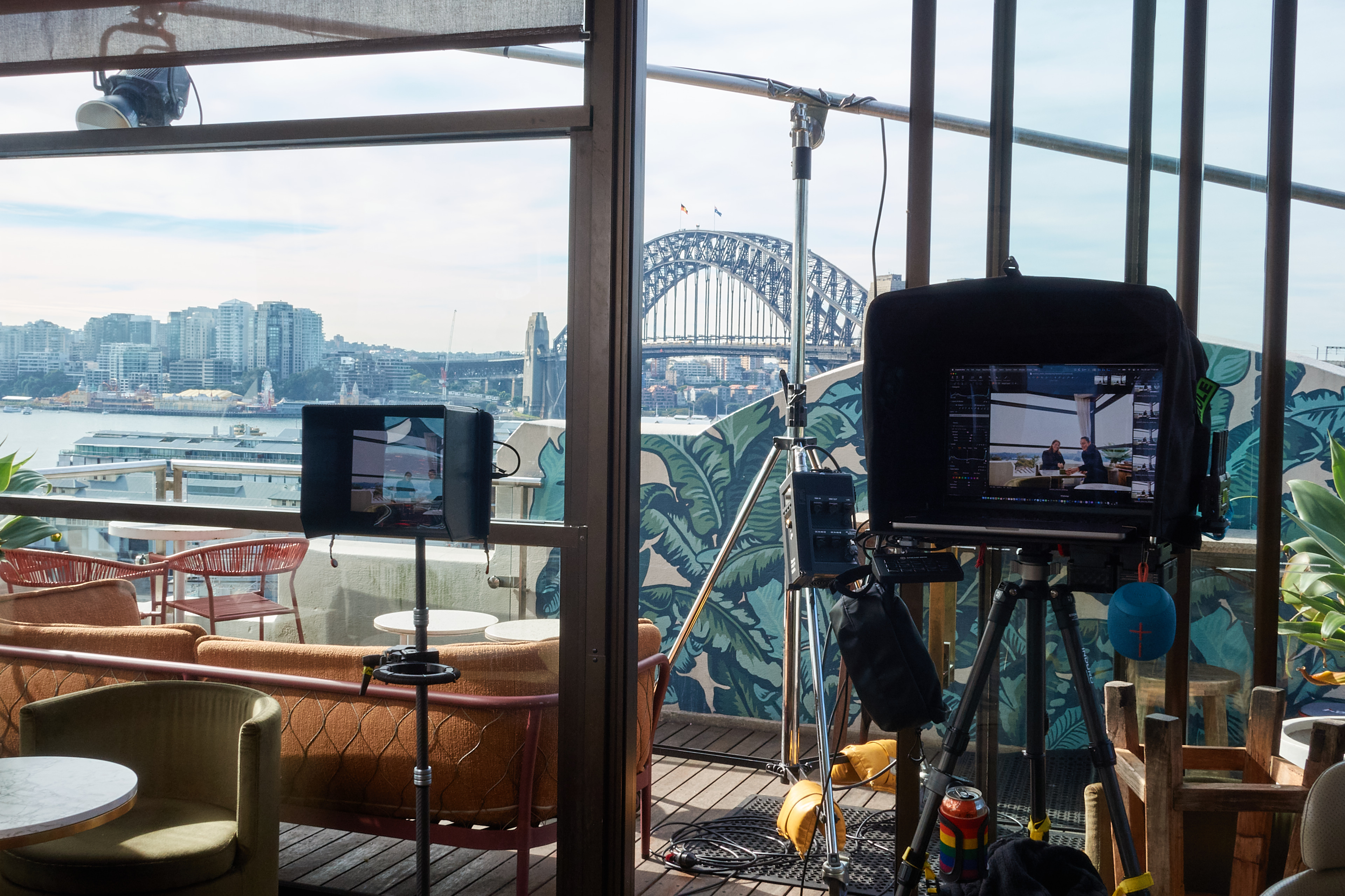 Behind-the-scenes shot with camera and lighting equipment set up on a rooftop overlooking the Sydney Harbour Bridge and city skyline.
