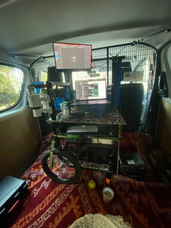 Interior view of a van converted into a mobile workstation with computer monitors, laptop, keyboard, and other accessories on a desk setup.