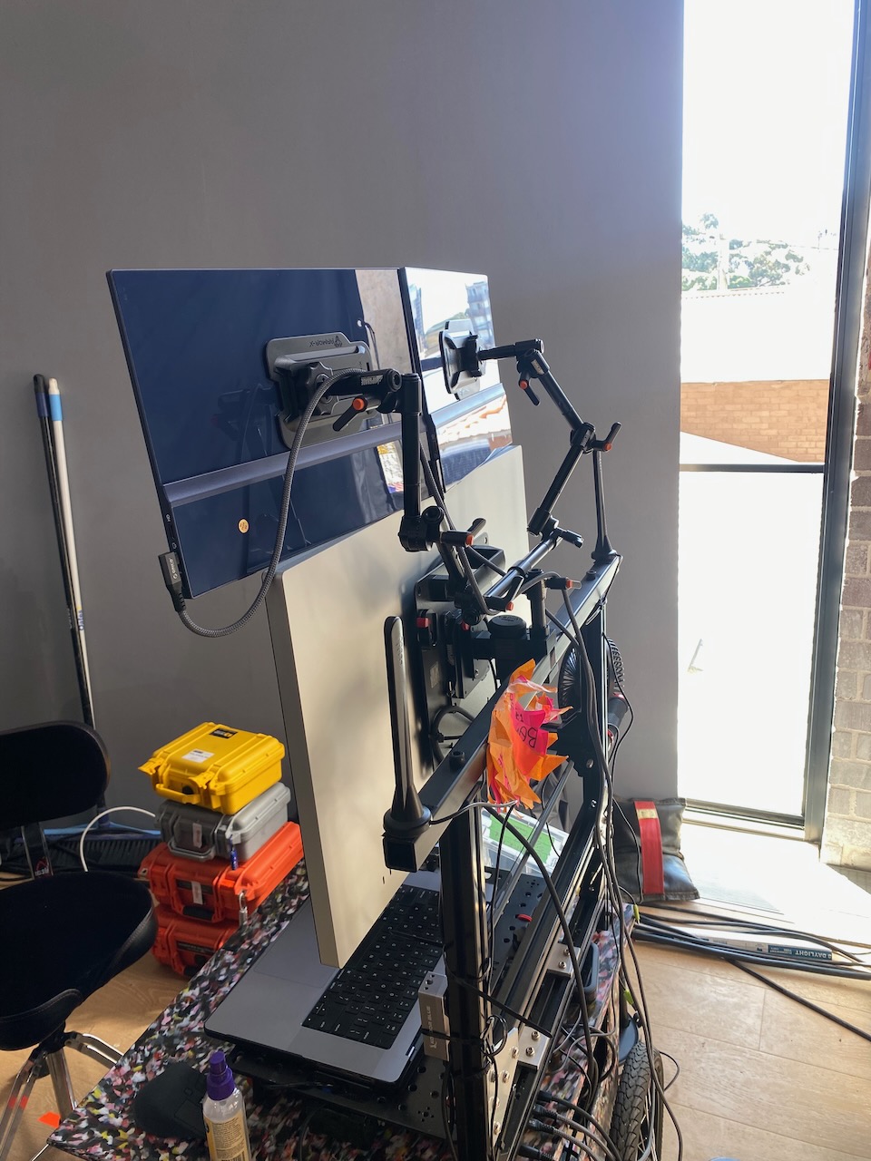 Image of a complex multi-monitor workstation setup with various computer accessories, power supplies, and wiring, in a bright, indoor room.