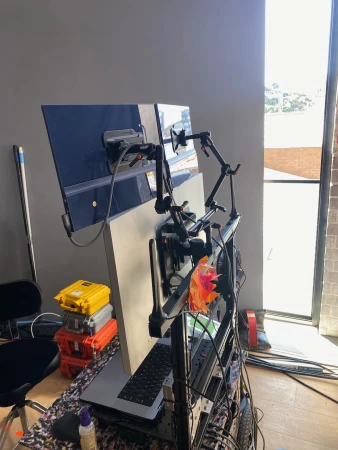 Image of a complex multi-monitor workstation setup with various computer accessories, power supplies, and wiring, in a bright, indoor room.