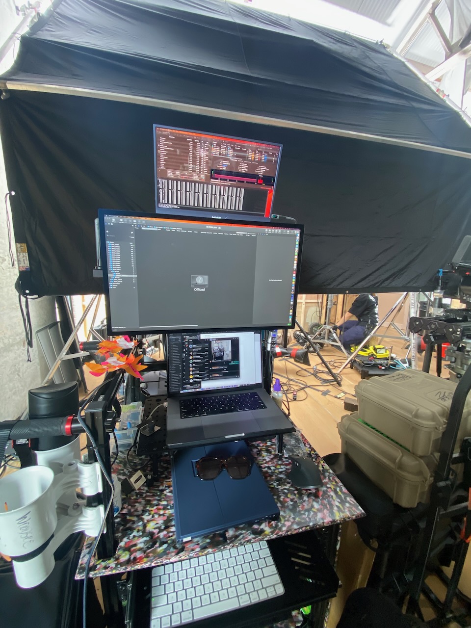 Behind-the-scenes of a video production workspace with two monitors, laptop, and accessories on a desk inside a temporary filming tent.