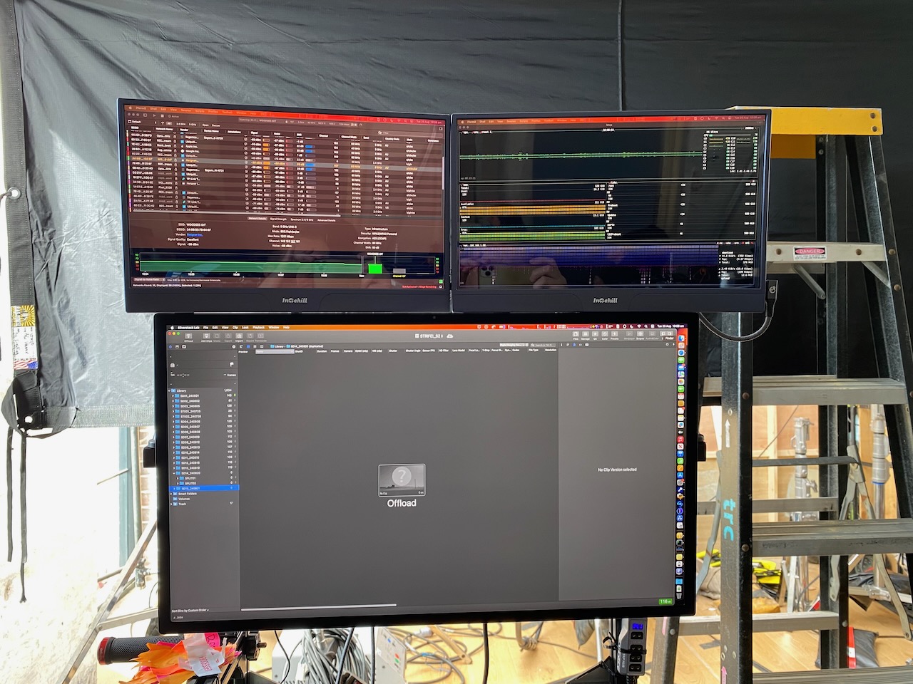 Multiple computer monitors displaying various interfaces, along with a ladder in what appears to be a production or technical environment.
